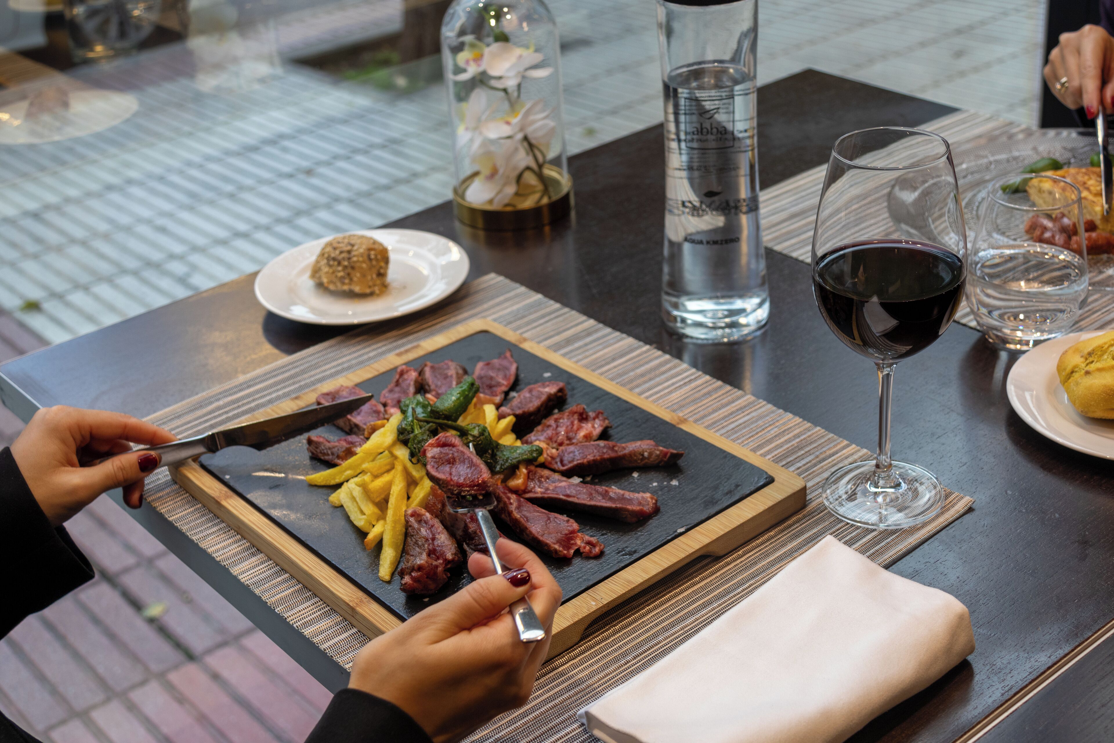 A dining table with a meal consisting of steak, fries, and a small dessert.