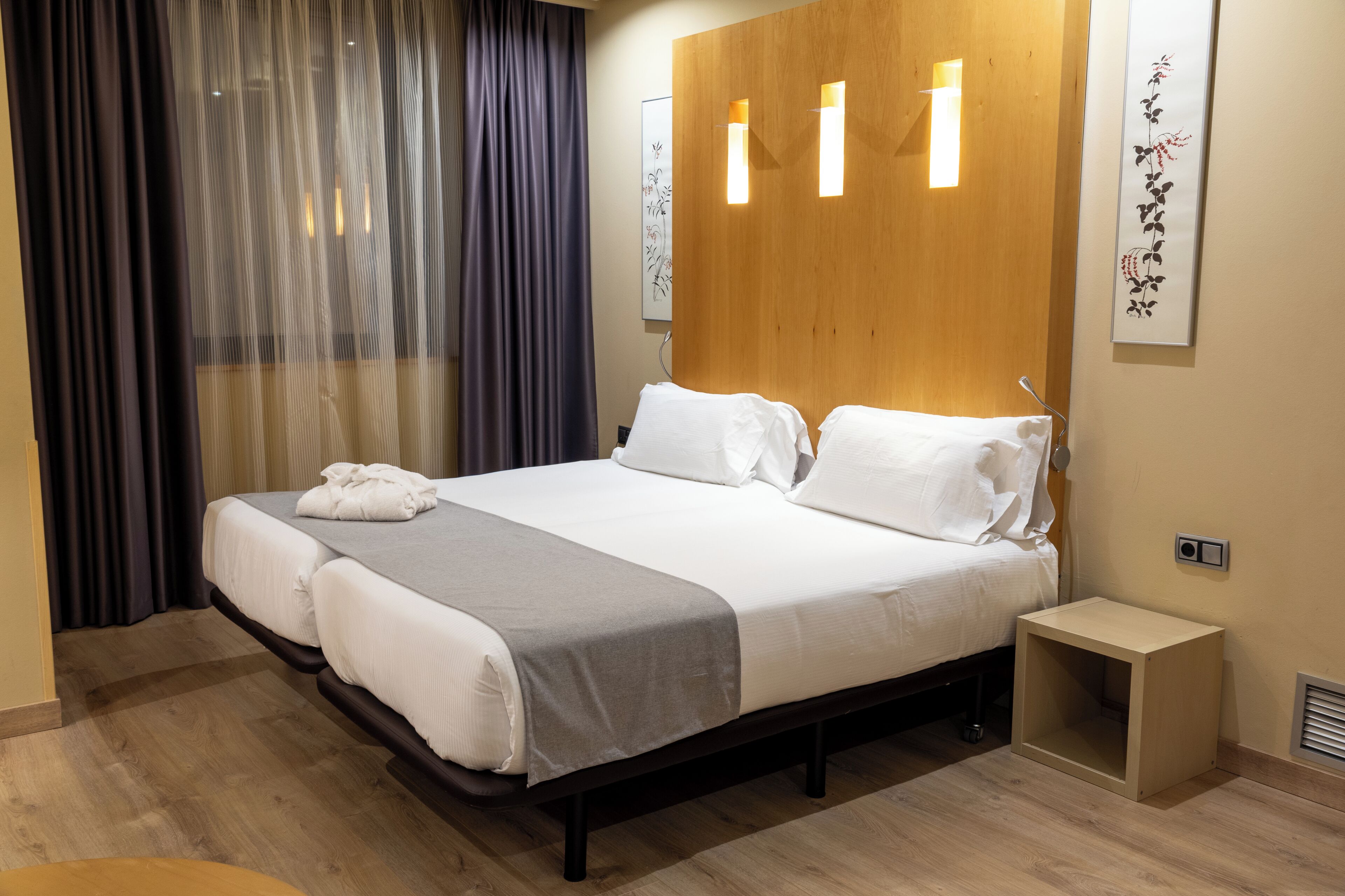 A neatly made bed with white linens and a gray throw blanket, a bedside table with a lamp, and a wooden headboard.