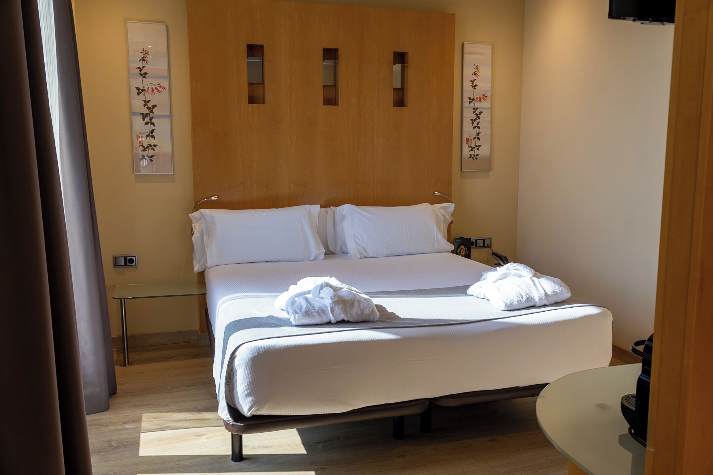 Een hotelkamer met een groot bed, twee kussens, een nachtkastje en een kunstwerk aan de muur.