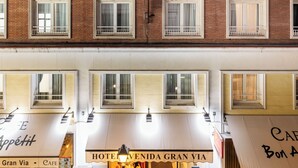 Fachada de hotel con múltiples ventanas, un café llamado "Café Bon Appetit" en la planta baja, y un cartel que dice "Hotel Venida Gran Via".