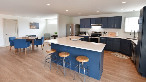 A modern kitchen with dark blue cabinets, a large island with stools, and a dining area with blue chairs. - Holiday Inn Express Wisconsin Dells by IHG (Baraboo)