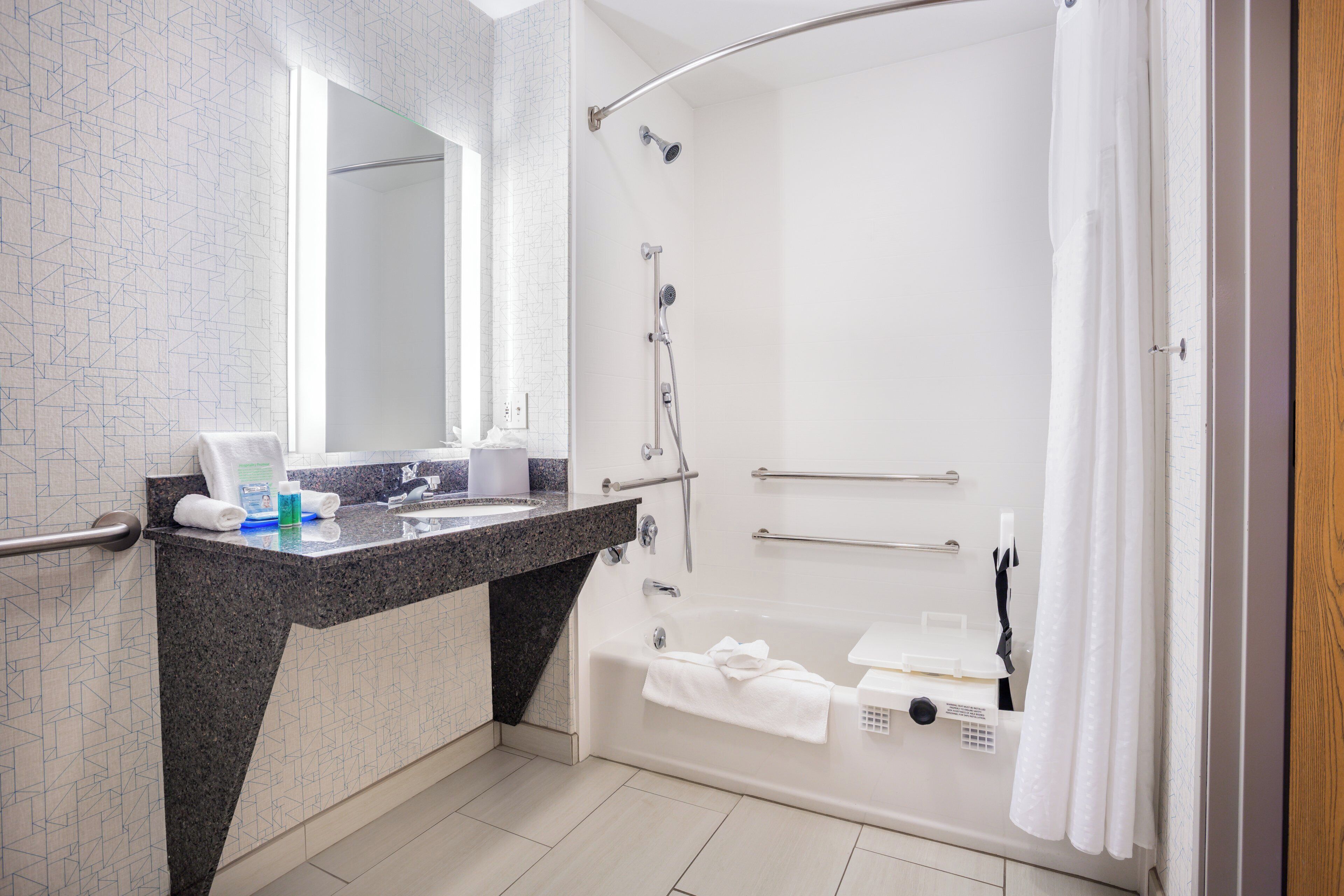 A modern bathroom with a granite countertop, a bathtub, a shower, and a large mirror.