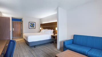 A hotel room with a bed, a desk, a chair, a blue sofa, and a wooden nightstand.