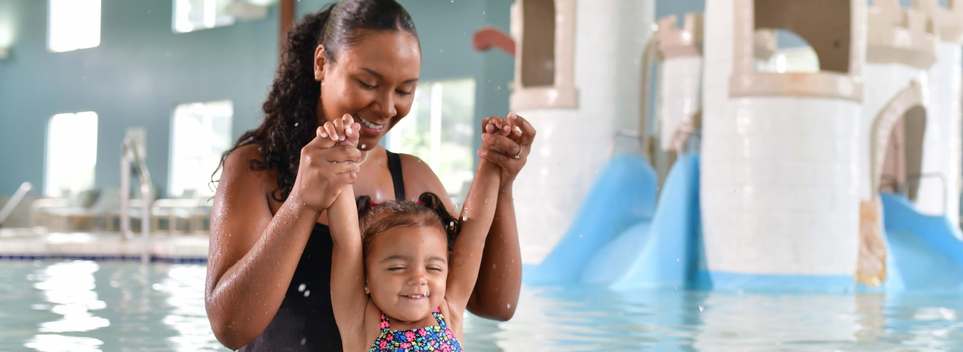 A woman and a child in a swimming pool with a water slide in the background.