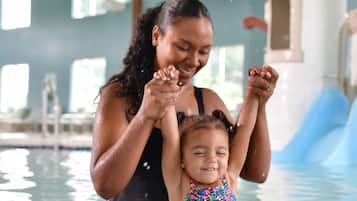 A woman and a child in a swimming pool with a water slide in the background.