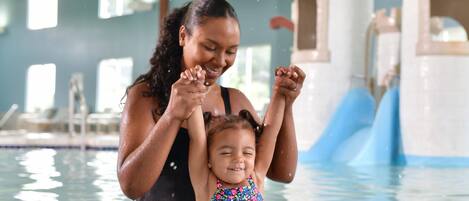 A woman and a child in a swimming pool with a water slide in the background.