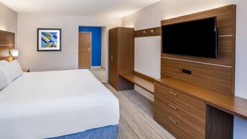 Een hotelkamer met een groot bed, een flatscreen televisie bevestigd aan een houten kast, een ingelijst kunstwerk aan de muur, en een blauwe deur op de achtergrond.