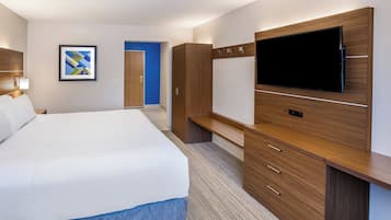 Quarto de hotel com cama, televisão, mobiliário de madeira, porta e quadro na parede.