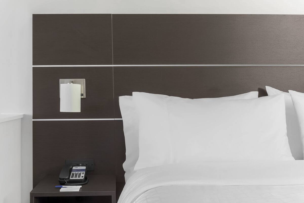 A hotel room with a bed, white linens, a nightstand with a phone, and a mirror.