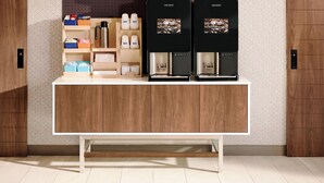 A modern coffee station with two coffee machines, a shelf with coffee cups, and a variety of coffee-related items. - Holiday Inn Express Wisconsin Dells by IHG (Baraboo)