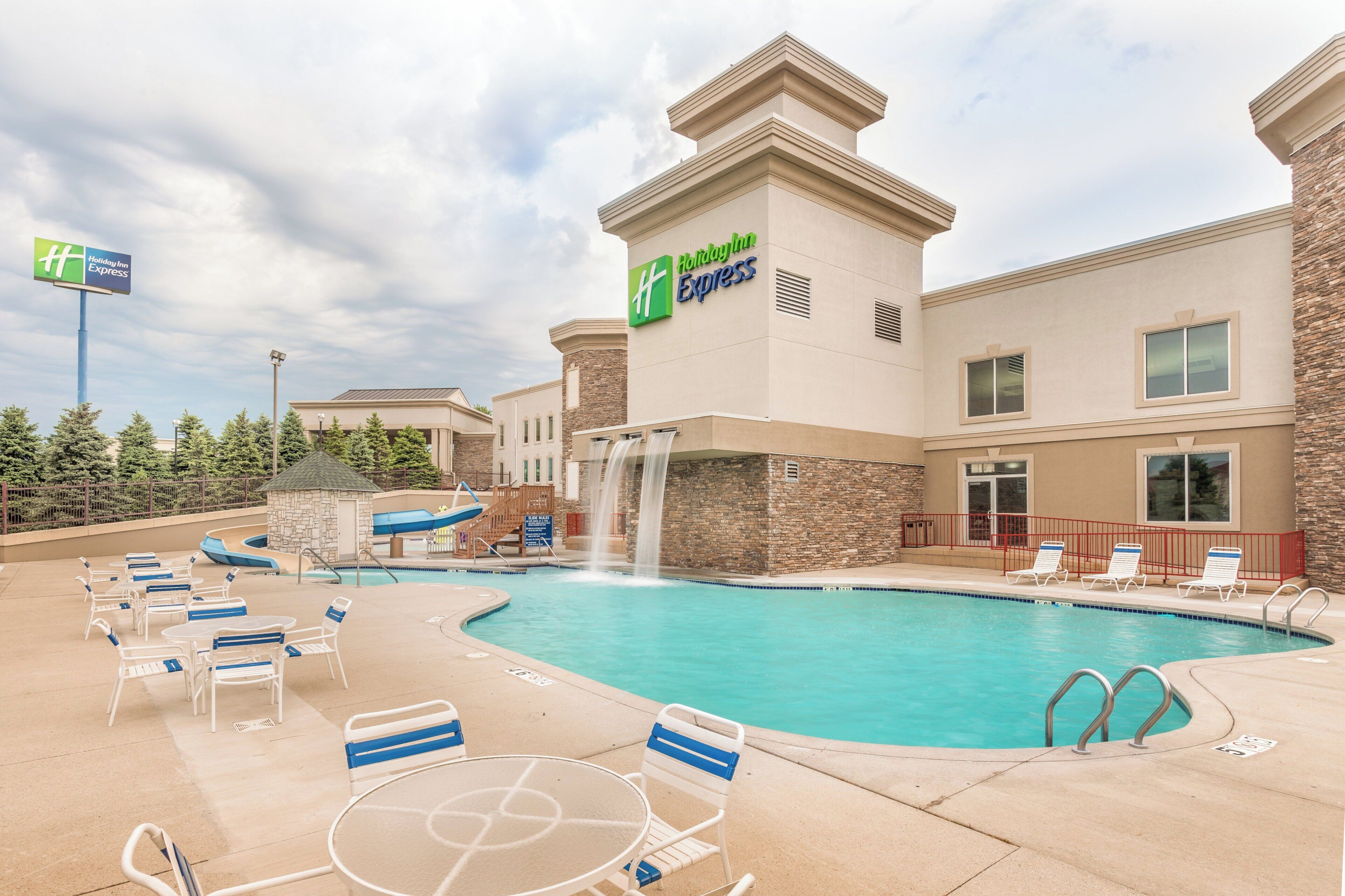 A Holiday Inn Express hotel with a swimming pool, lounge chairs, and a waterfall feature.