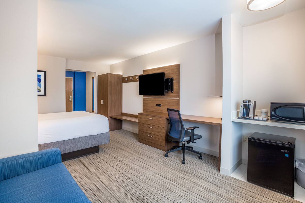 A hotel room with a bed, a desk with a chair, a television, a coffee maker, a microwave, and a mini-fridge.