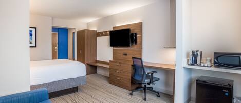 A hotel room with a bed, a desk with a chair, a television, a coffee maker, a microwave, and a mini-fridge.