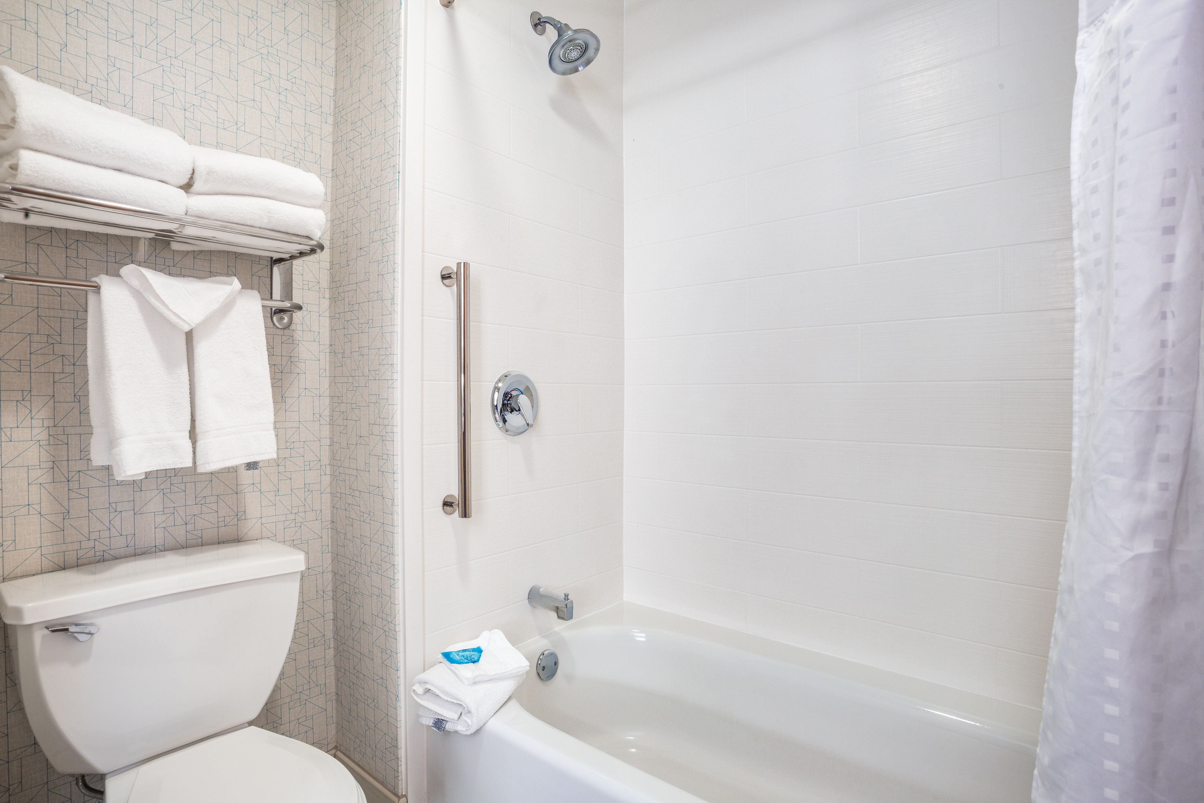 A bathroom with a toilet, a bathtub, and a shower. There are towels on a rack and a towel on the floor.