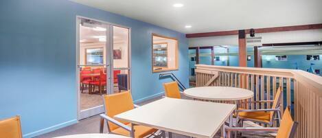 A hotel room with a blue wall, a white table, and orange chairs.
