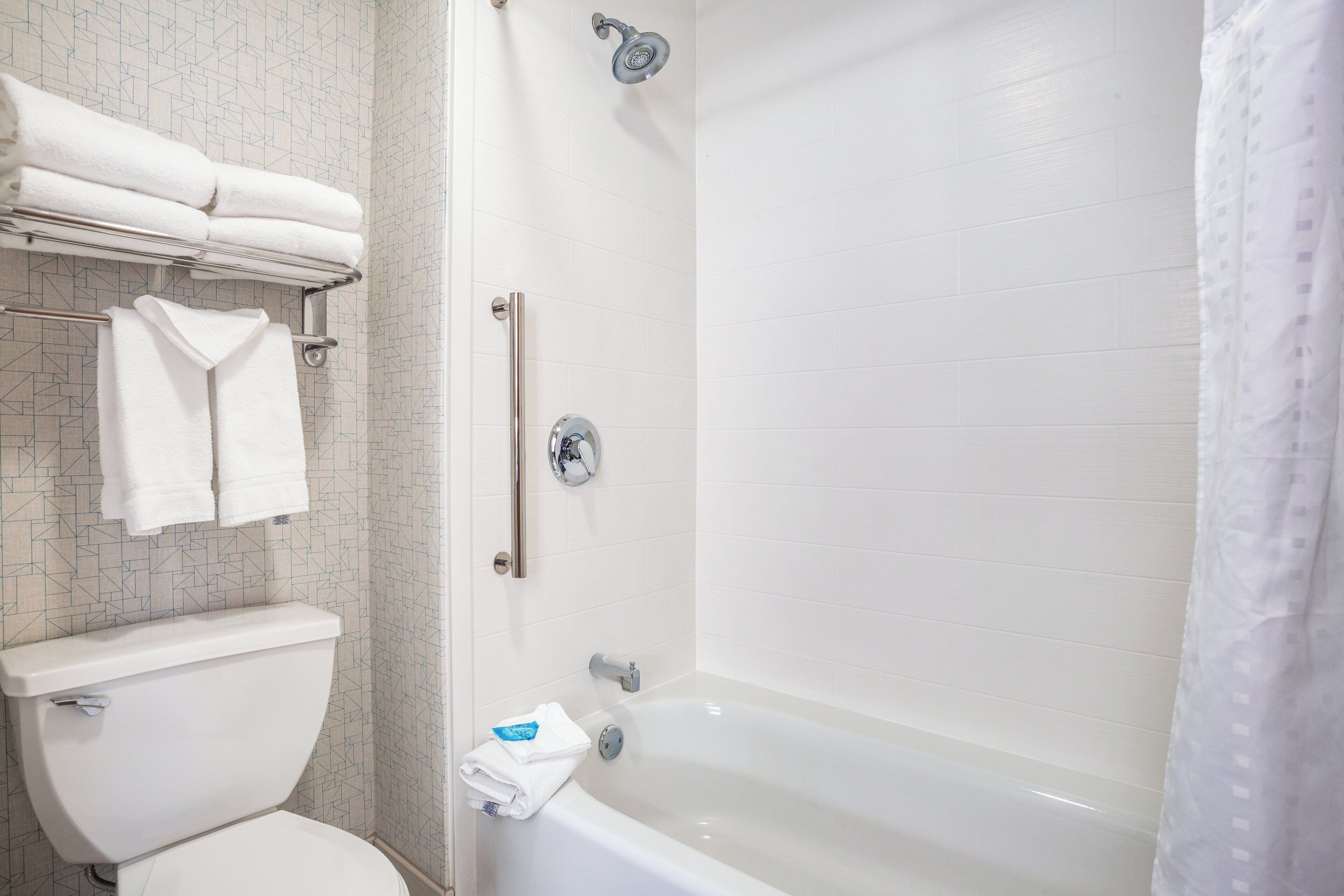 Une salle de bain comprenant des toilettes, une douche avec une porte en verre et un porte-serviettes avec des serviettes pliées.