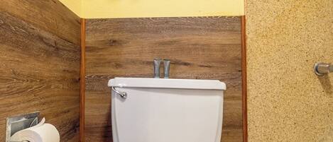 A bathroom with a toilet, a towel rack with three towels, a wooden wall, and a bathtub.