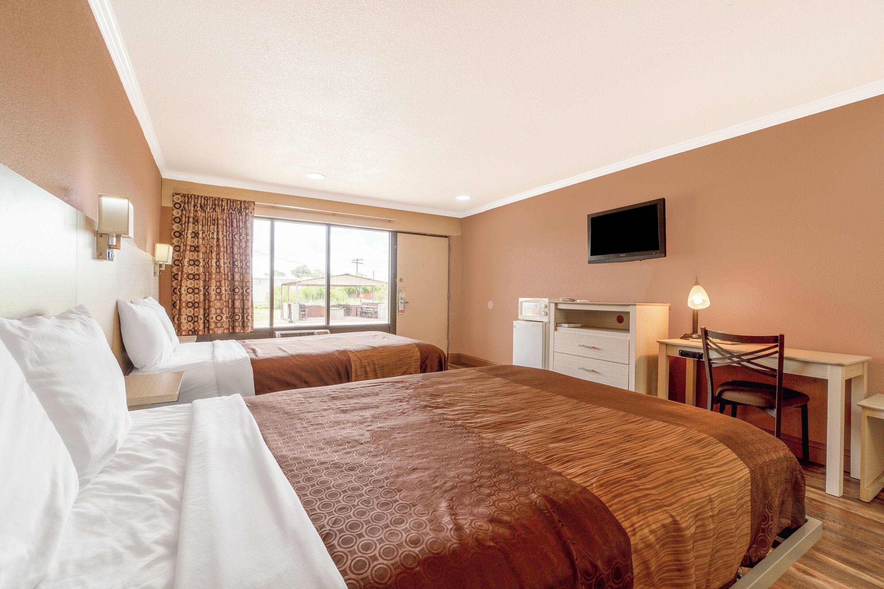 Habitación de hotel con dos camas, un escritorio con silla, televisor y ventana con cortinas.