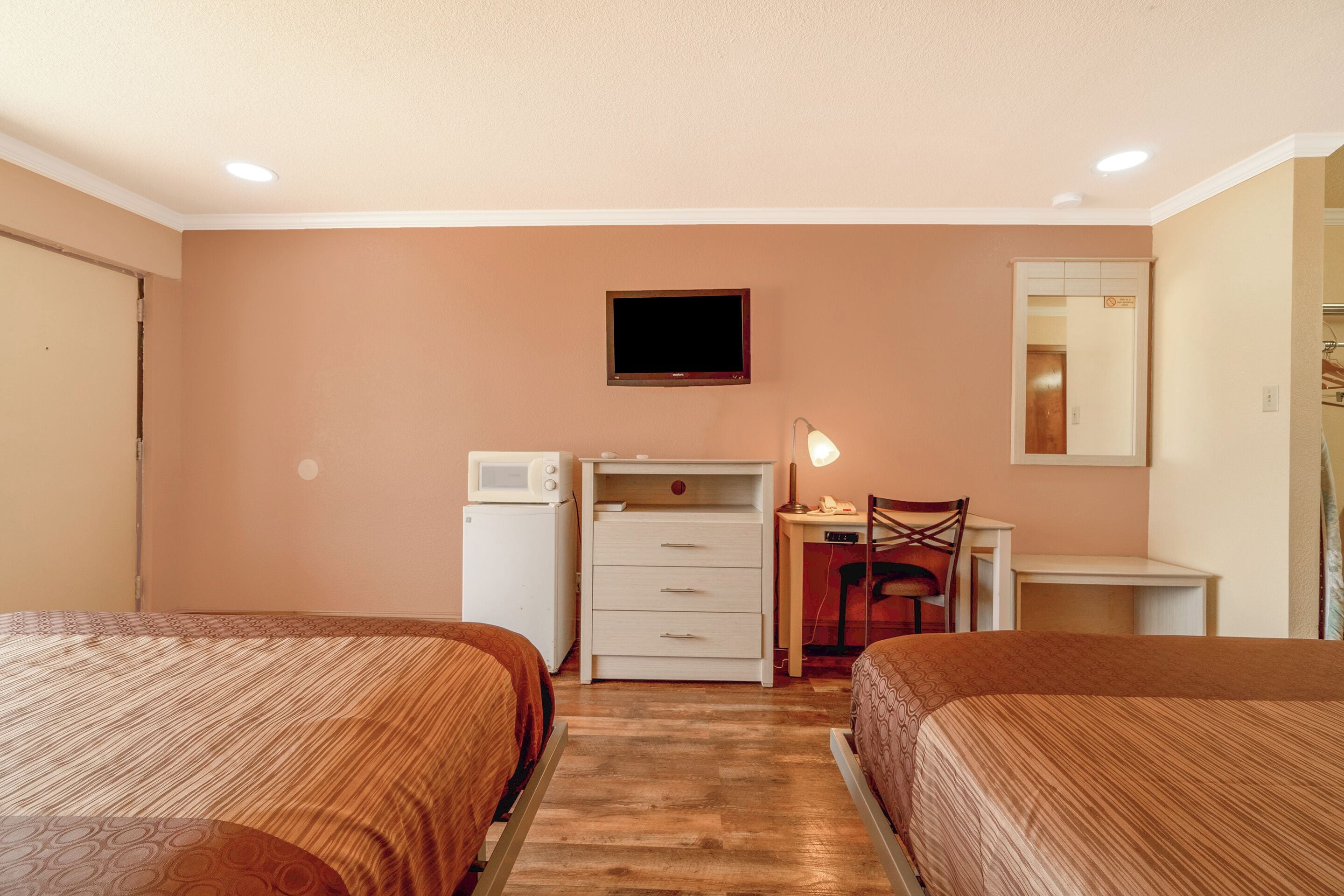 Habitación de hotel con dos camas, un escritorio, una silla, un televisor, una lámpara de escritorio y un microondas.