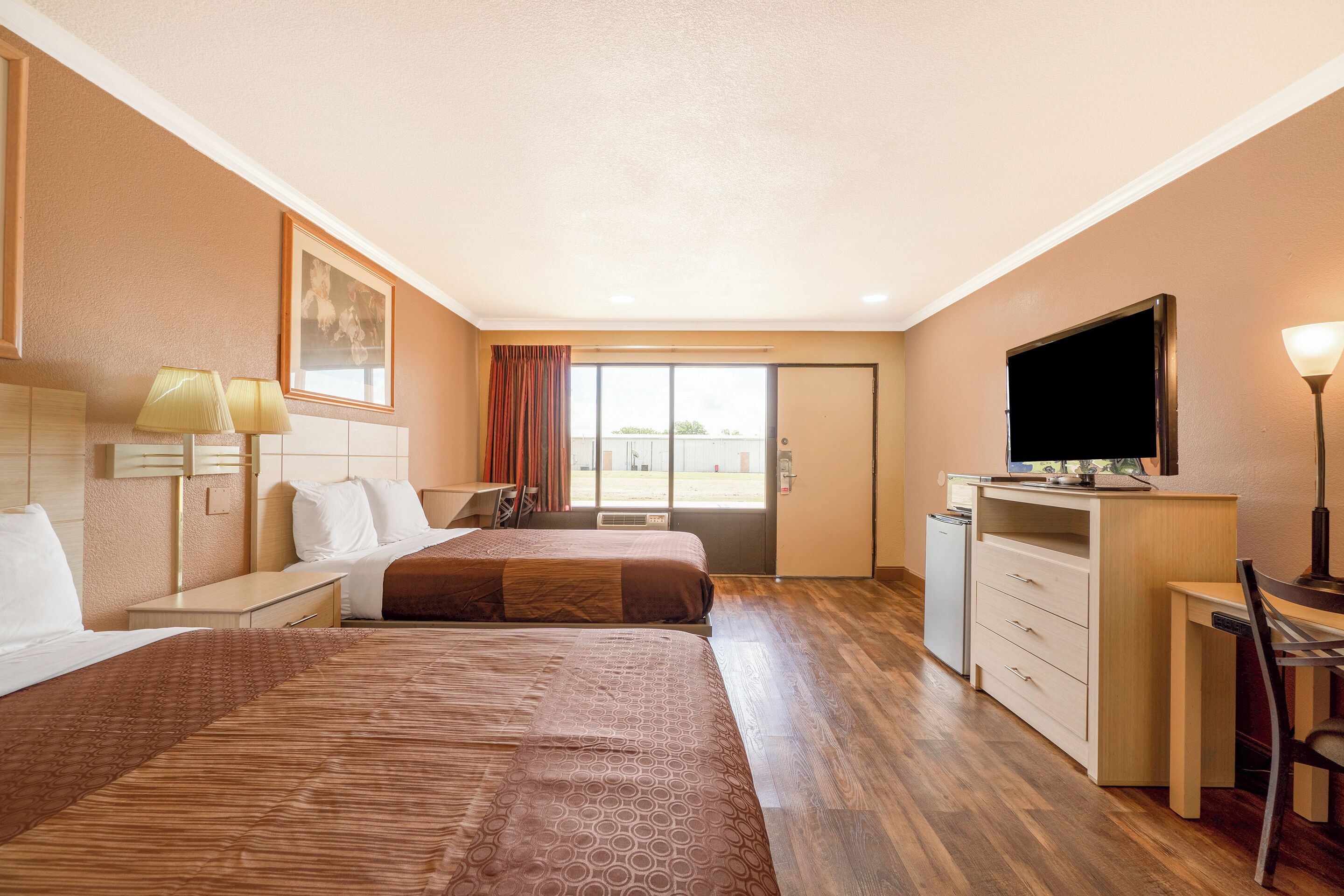 Una habitación de hotel con dos camas, un escritorio, un televisor y una ventana con vistas.