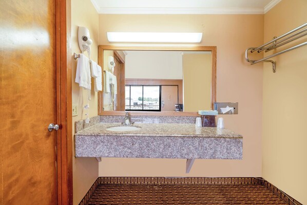 A bathroom with a granite countertop sink, a mirror, a hairdryer, and a towel rack.