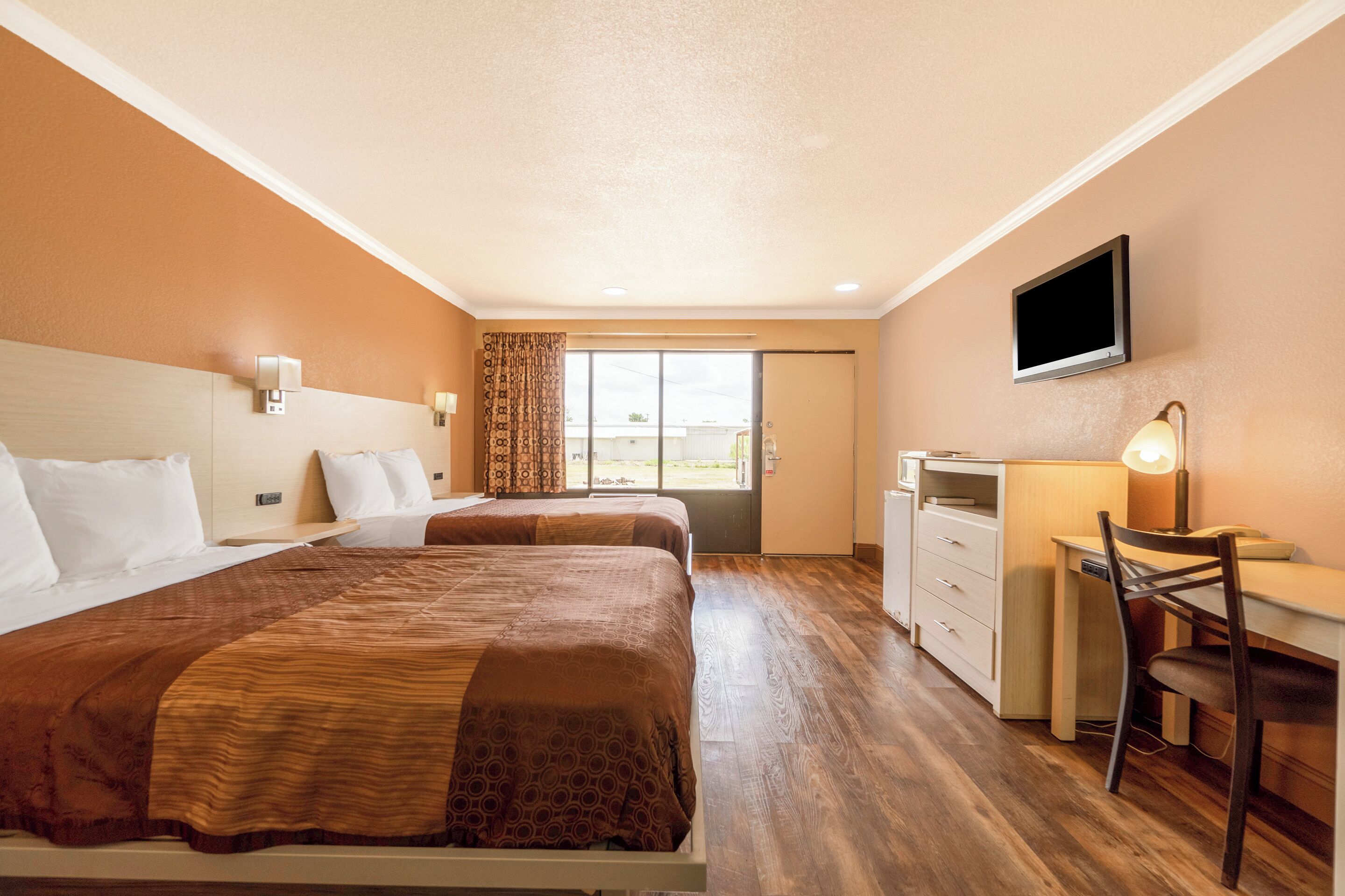 A hotel room with two beds, a desk, a chair, a TV, and a window with curtains.