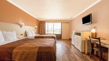 A hotel room with two beds, a desk, a chair, a TV, and a window with curtains.