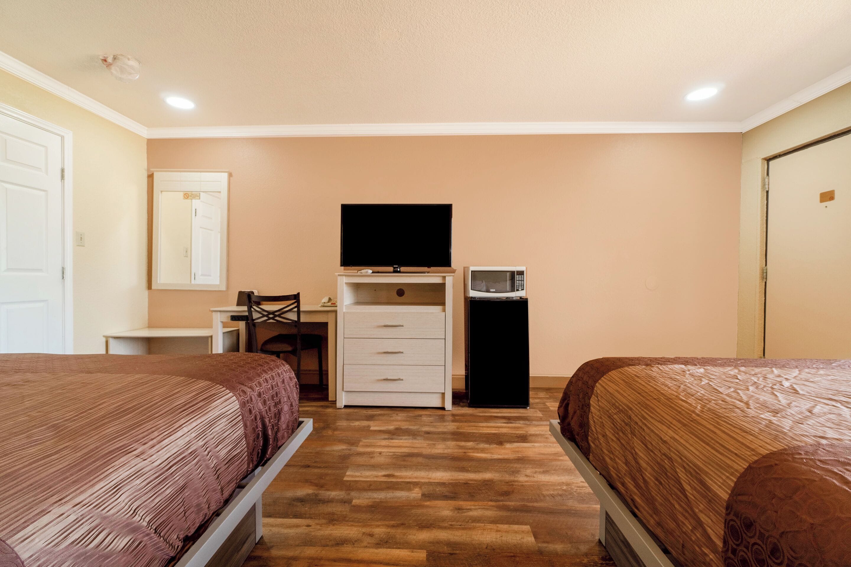 A bedroom with two beds, a desk, a chair, a television, and a microwave.