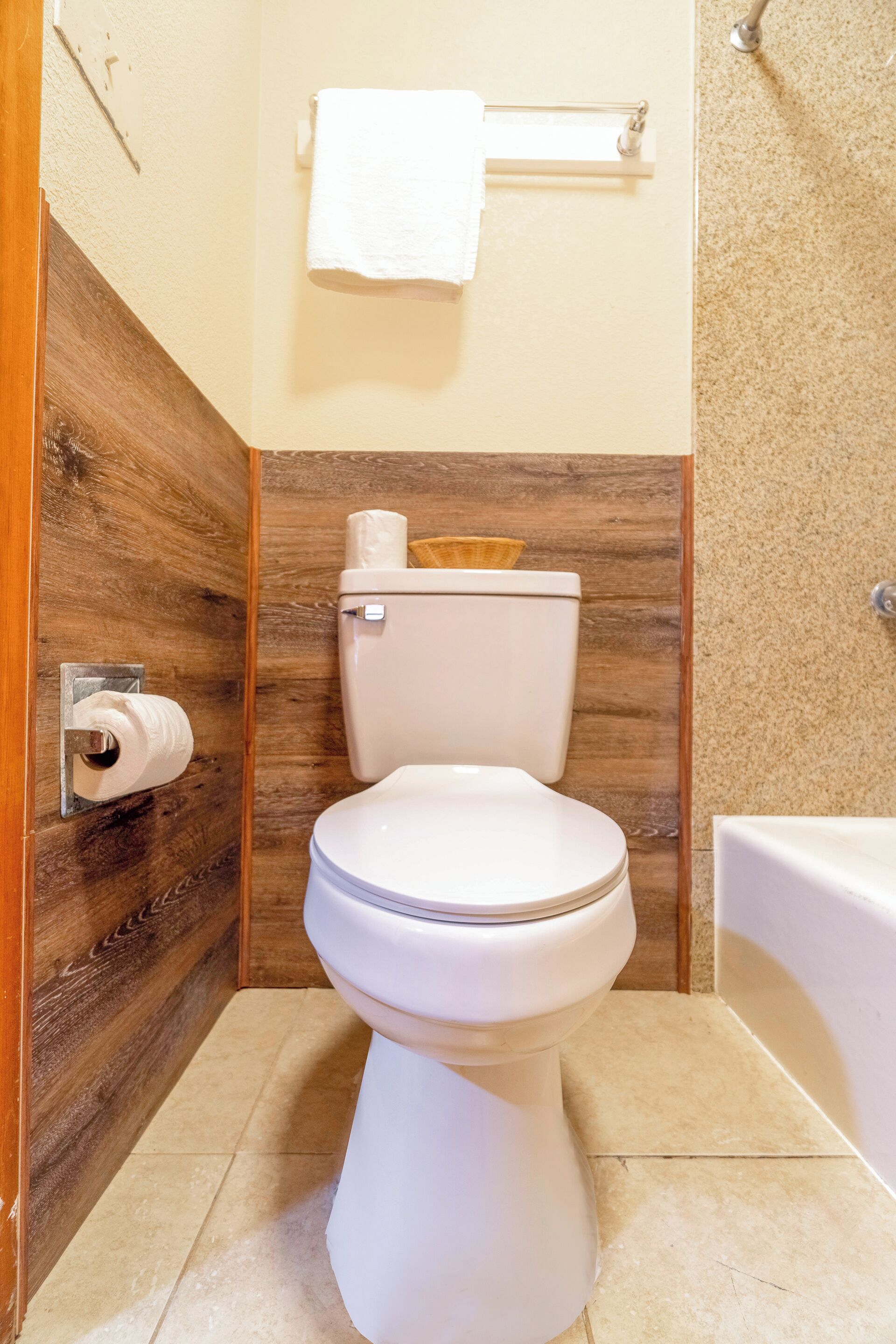 A bathroom with a toilet, a roll of toilet paper, a towel rack, and a bathtub.