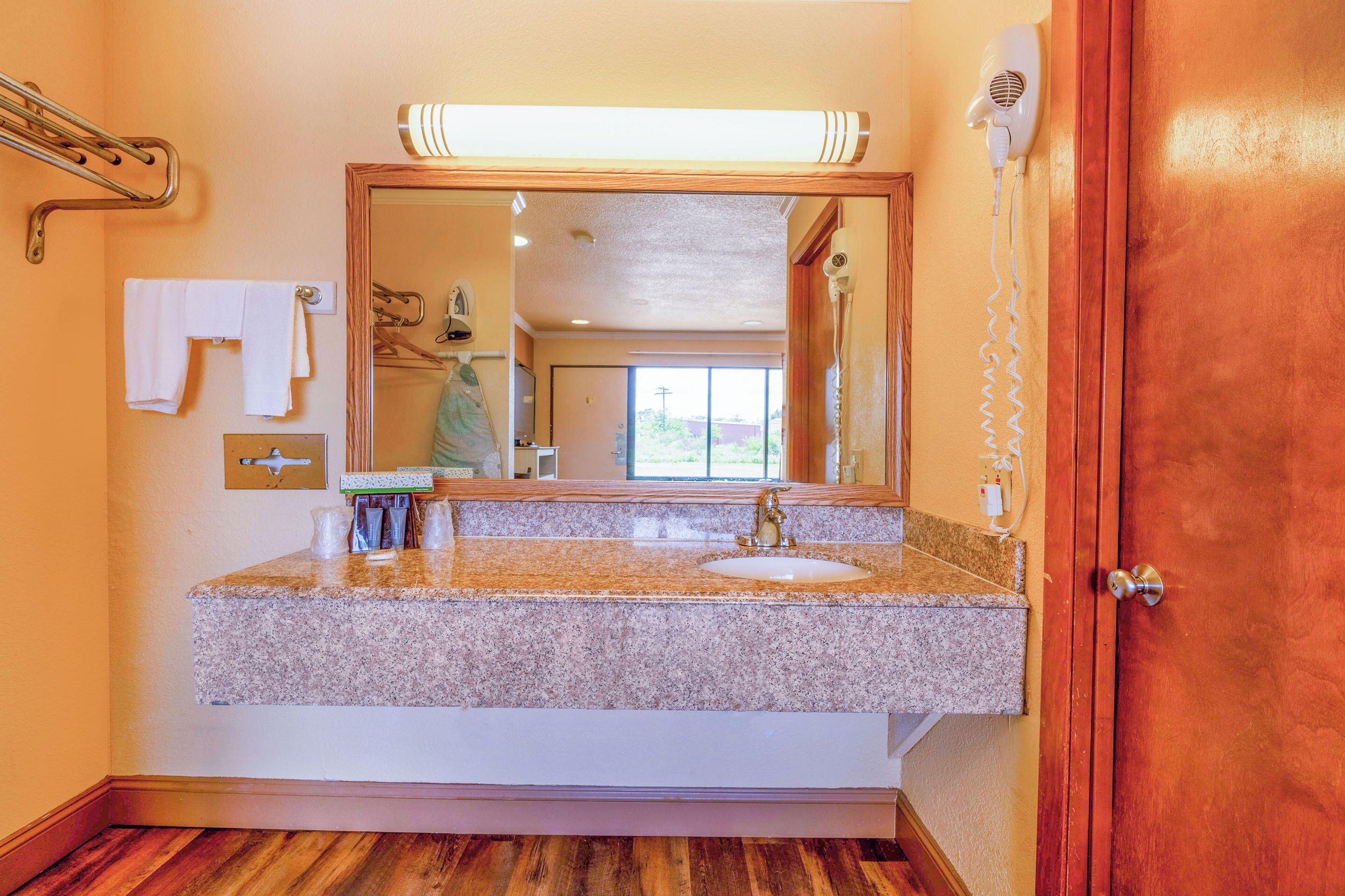 A bathroom with a granite countertop sink, a large mirror, a towel rack, and a hairdryer mounted on the wall.