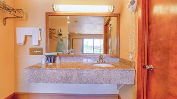 A bathroom with a granite countertop sink, a large mirror, a towel rack, and a hairdryer mounted on the wall.