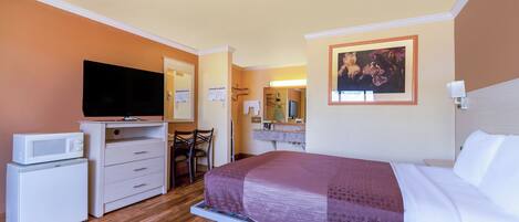 A hotel room with a bed, a television, a microwave, a refrigerator, a desk, and a chair.