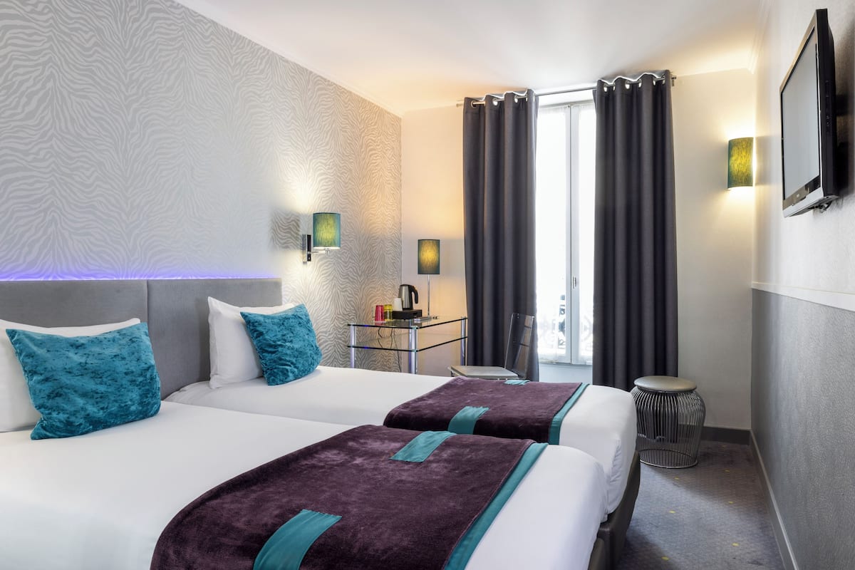 Een hotelkamer met twee bedden, een kleine tafel met een lamp, een televisie en uitzicht op het omliggende landschap.