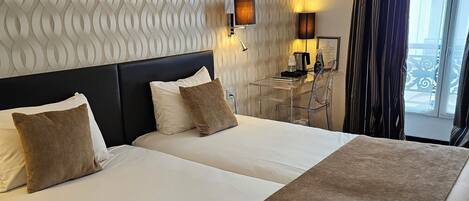 A hotel room with two beds, a patterned wall, a nightstand with a lamp, and a view of the outdoors.