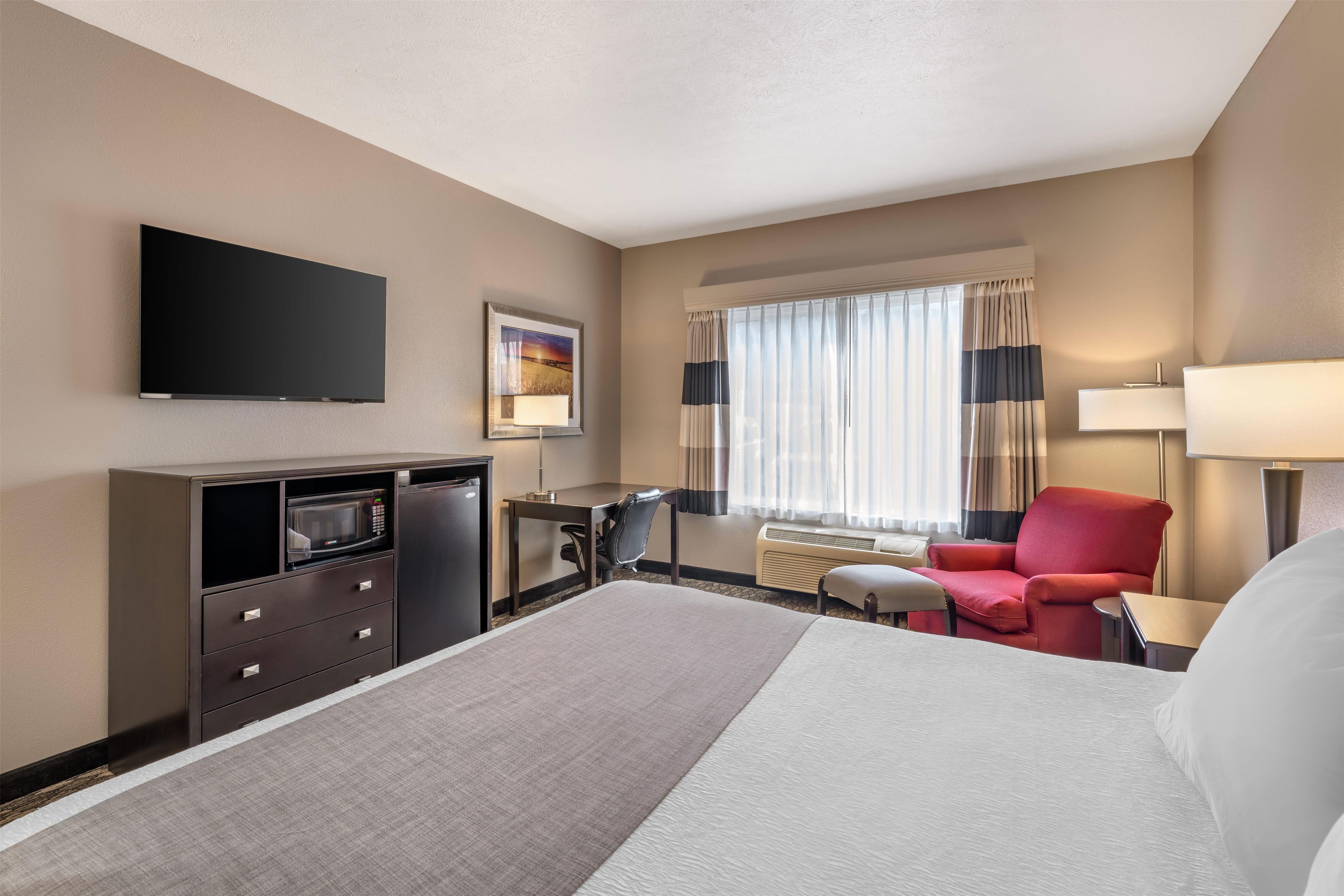 A hotel room with a bed, a desk, a chair, a TV, a microwave, and a window with curtains.