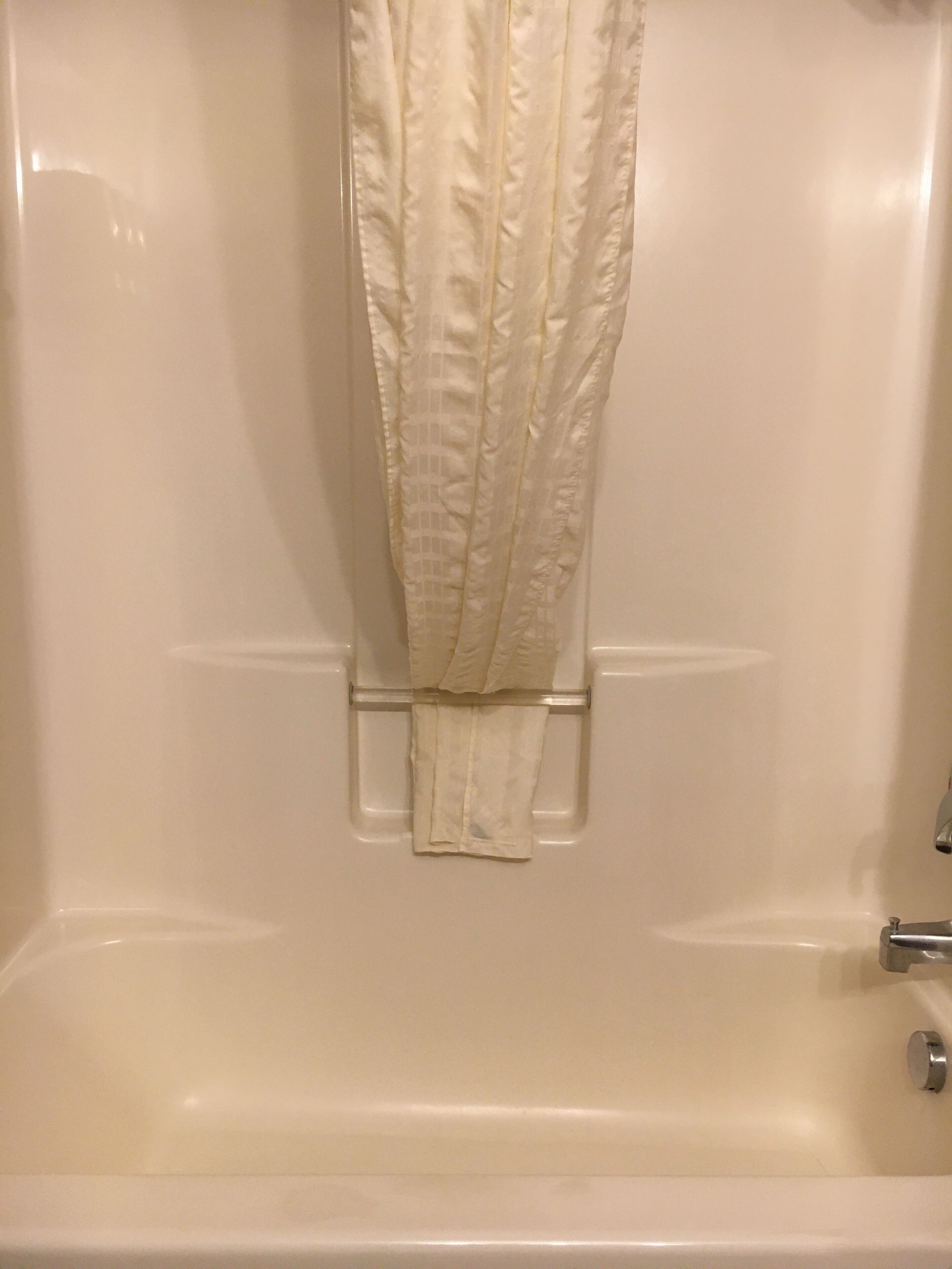 A bathtub with a white curtain and a towel rack.