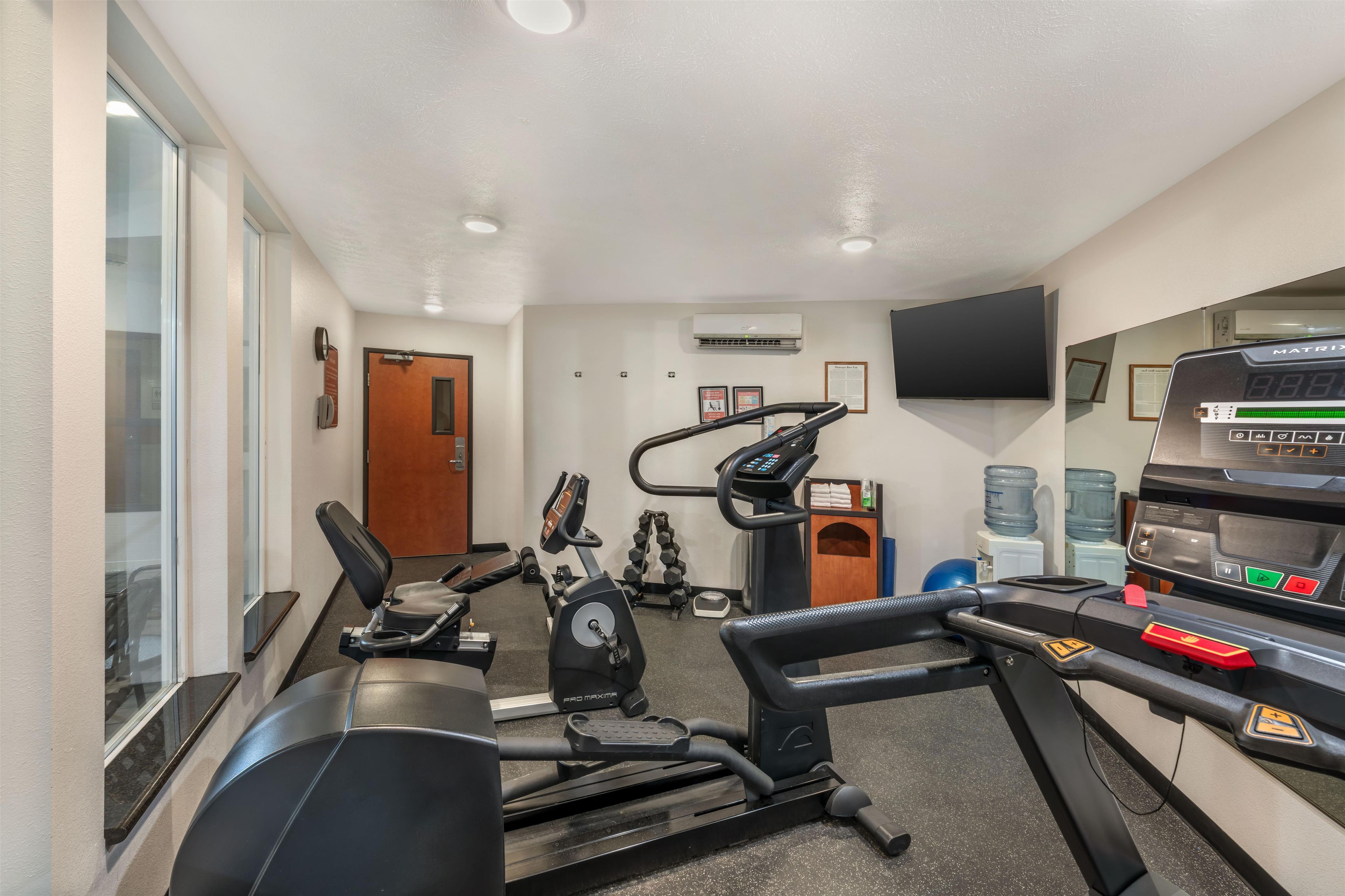 Academia com equipamentos de cardio, pesos e televisão.