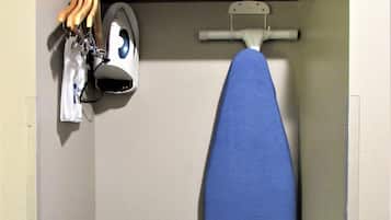 A small laundry area with an iron, ironing board, and hanging clothes.