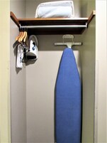 A small laundry area with an iron, ironing board, and hanging clothes.