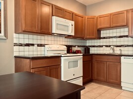 Una cocina con armarios de madera, una estufa blanca, un microondas y un salpicadero de azulejos.