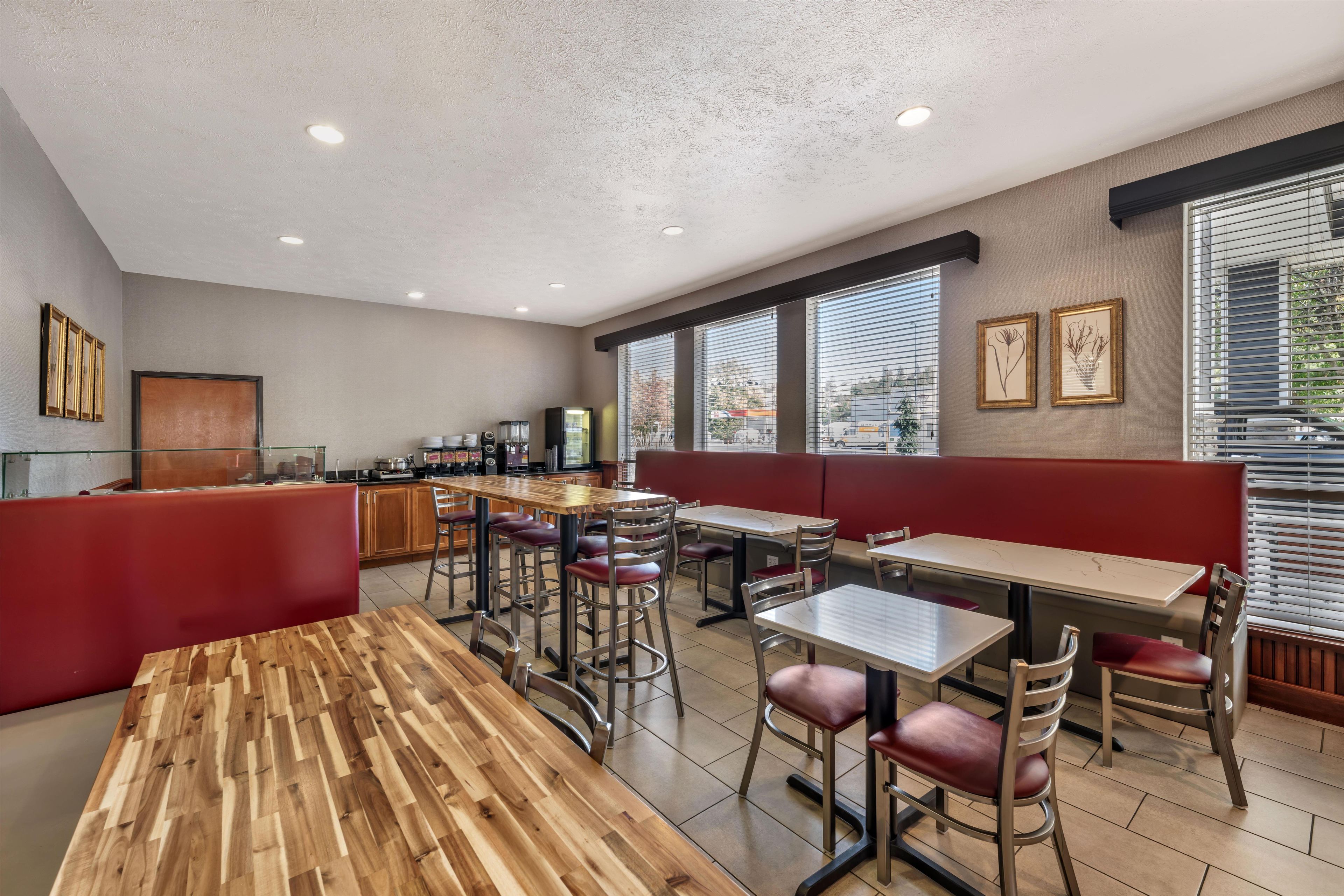 A restaurant with wooden tables and red booths, a kitchen area, and large windows with blinds.