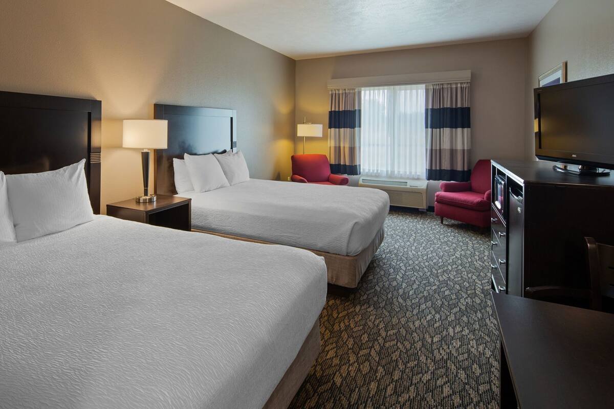 A hotel room with two beds, a TV, a desk, and a window with curtains.