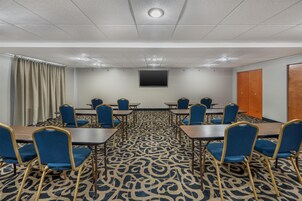Un salón de conferencias con alfombra estampada, sillas azules y una pantalla grande en la pared.