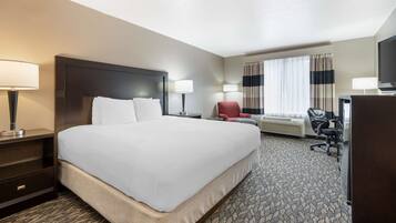 A hotel room with a large bed, two bedside tables with lamps, a desk with a chair, a TV, and a window with curtains.