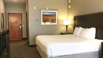 A hotel room with a large bed, a nightstand with a lamp, a framed picture on the wall, and a door to the left.