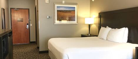 A hotel room with a large bed, a nightstand with a lamp, a framed picture on the wall, and a door to the left.