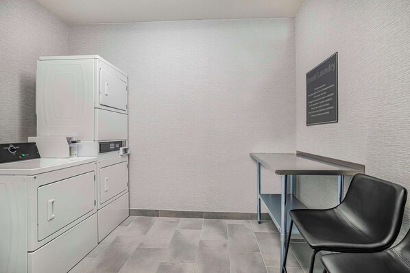 Un área de lavandería con lavadora, secadora y una mesa con una silla.