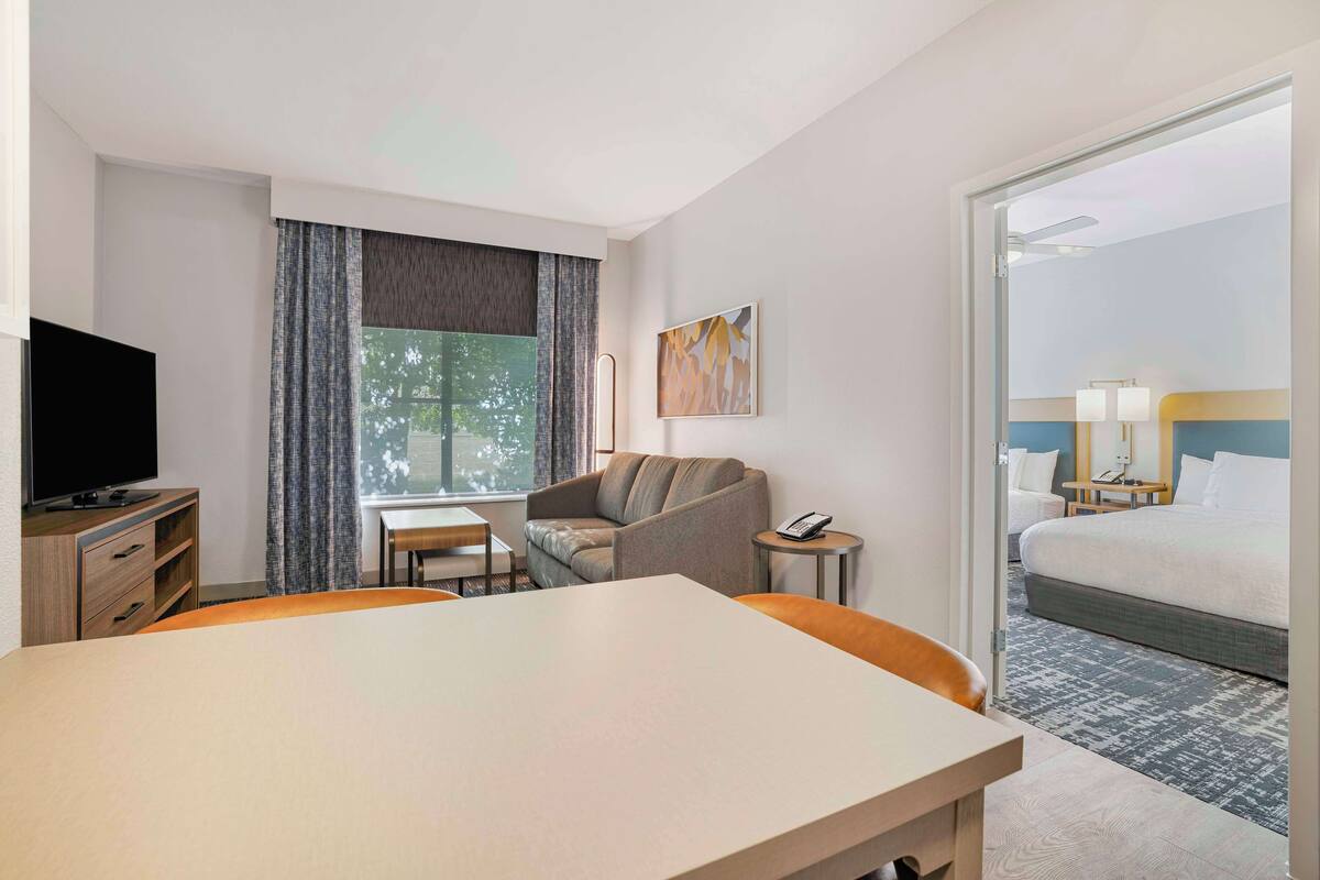 A hotel room with a bed, a desk, a television, a sofa, a chair, a small table, and a window with curtains.