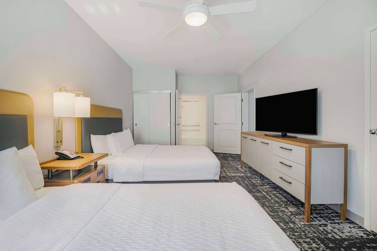 A hotel room with a large bed, a desk with a lamp, a television, and a wardrobe.