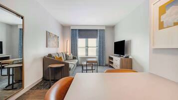 Een moderne hotelkamer met een bank, een eettafel, een televisie en een grote spiegel.